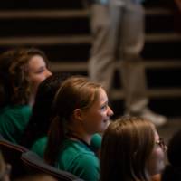 students in green T-shirts sit in auditorium